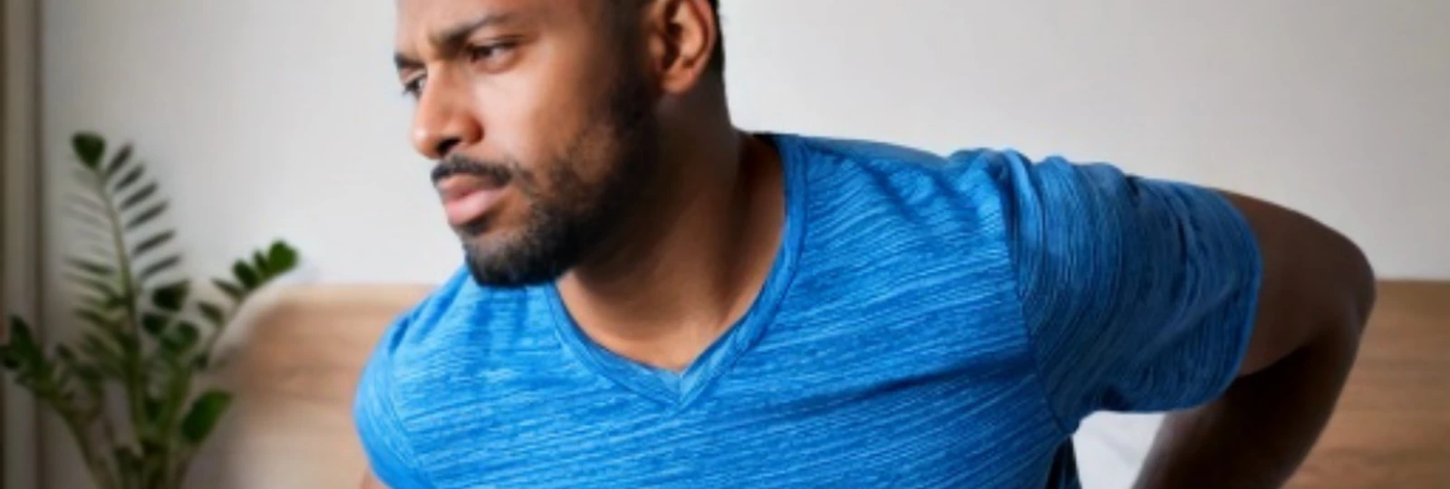 Man in blue t-shirt holding lower back.